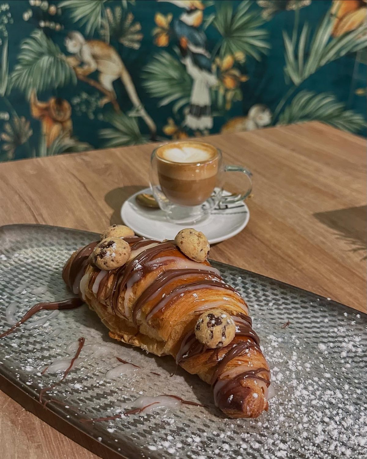 Café con leche y croissant de chocolate ante el papel pintado tropical