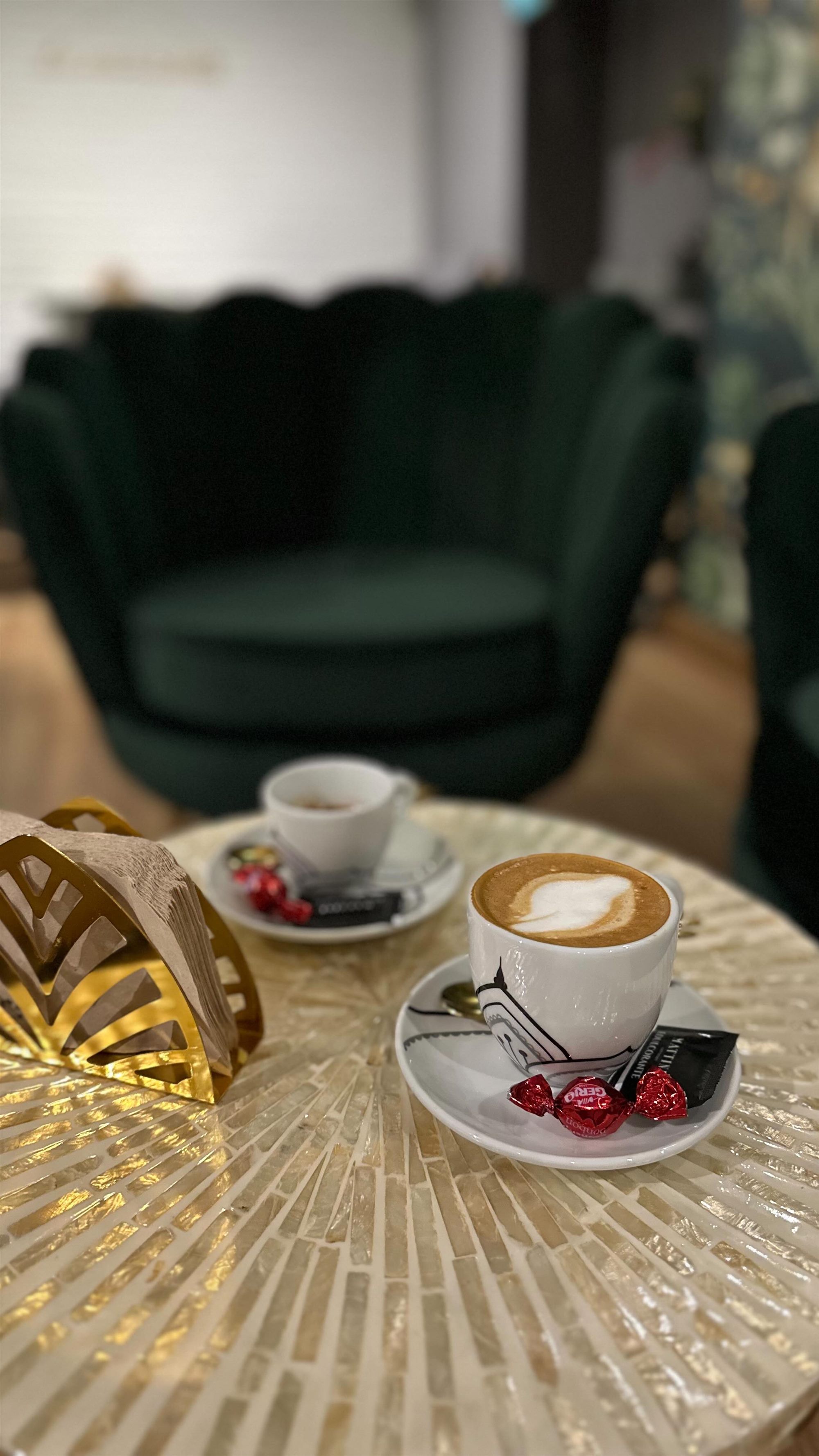 Espresso sobre mesa dorada junto a una butaca de terciopelo verde
